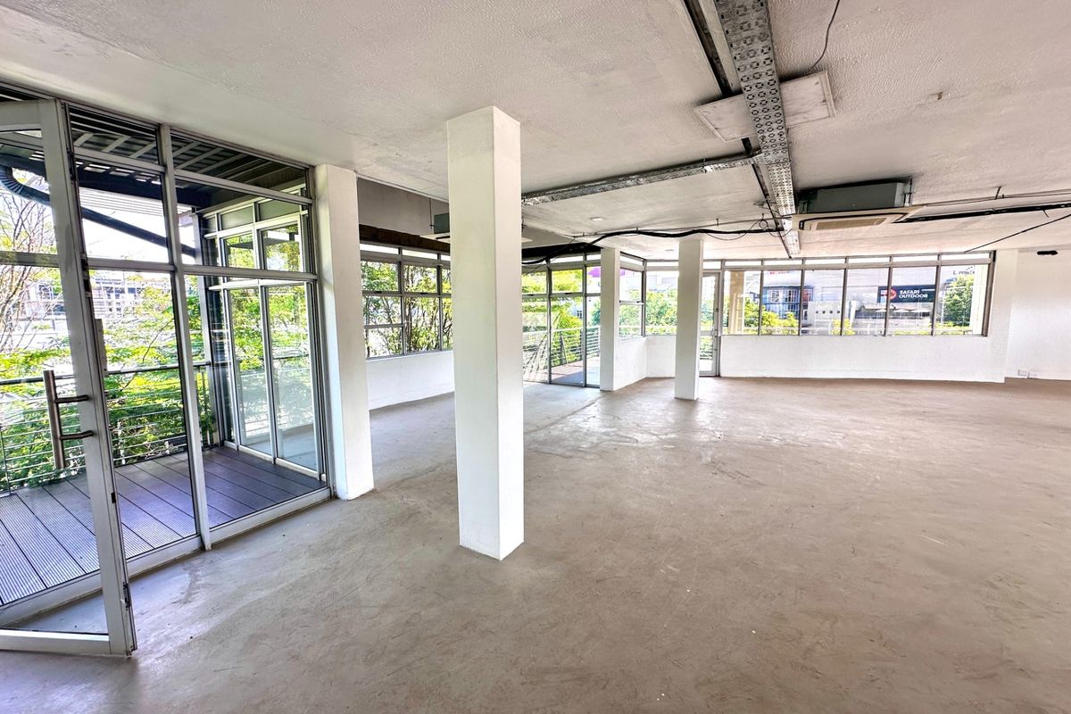 Spacious, open-plan office area featuring exposed ceiling cable trays, large windows for natural light, and direct access to a private balcony.