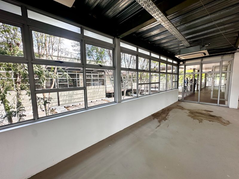 A bright, open-plan office corridor featuring large windows, exposed industrial ceiling details, and glass-panelled access doors.