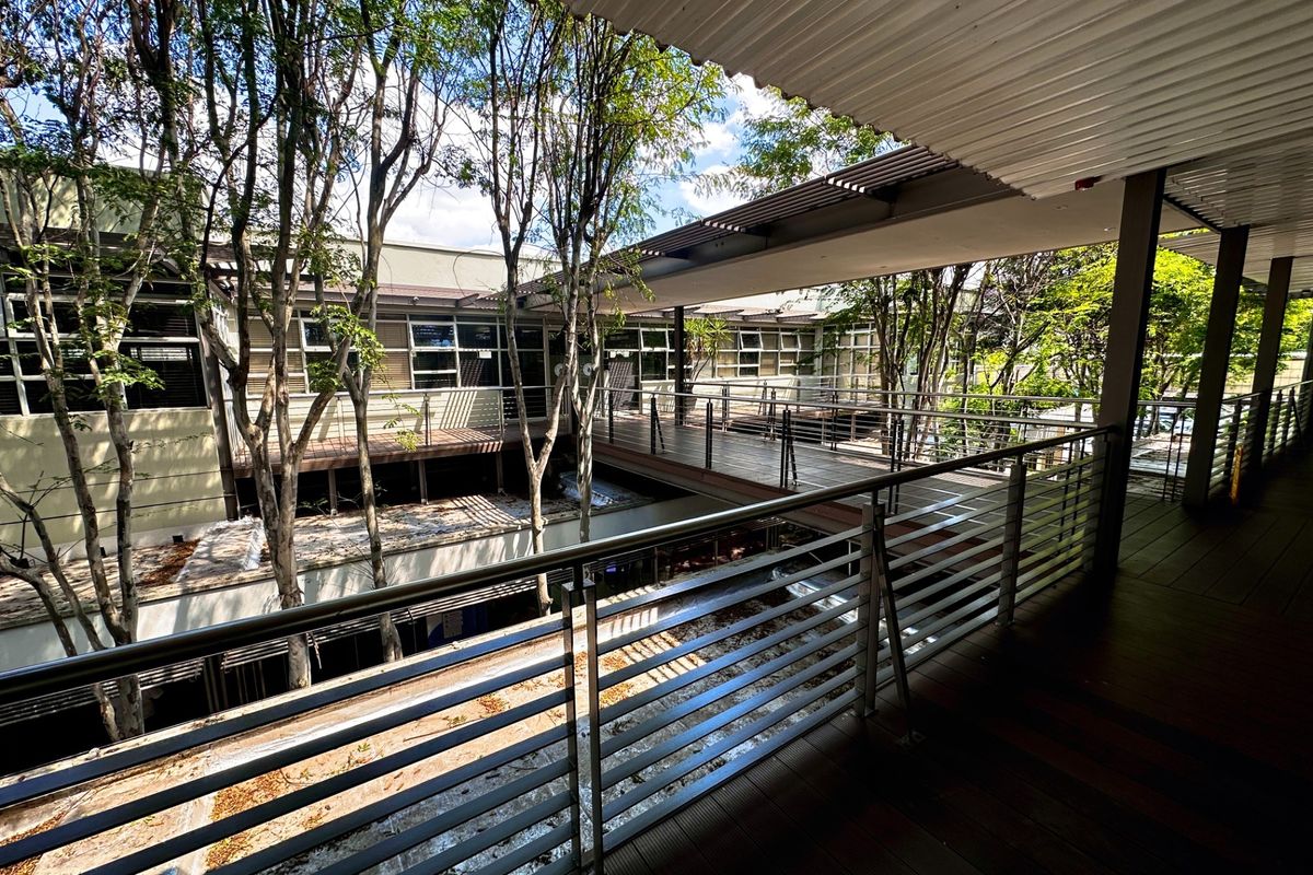An elevated outdoor walkway and balcony area featuring timber decking, metal balustrades, and a covered roof structure overlooking a landscaped courtyard.