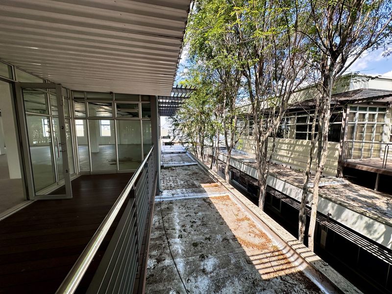 An elevated outdoor balcony featuring timber decking and metal balustrades, providing access to office interiors through large glass sliding doors.