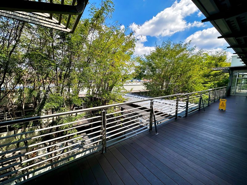 A spacious, modern balcony featuring composite decking and a sleek stainless steel railing, overlooking a lush, tree-filled outdoor area.