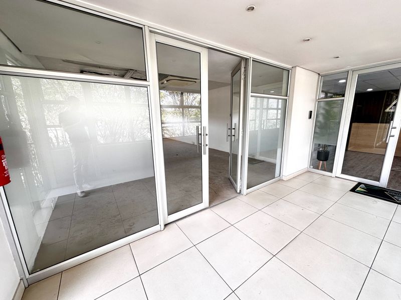 A bright, empty office space featuring modern glass partitions, aluminum framing, and clean tiled flooring, suitable for a professional workspace layout.