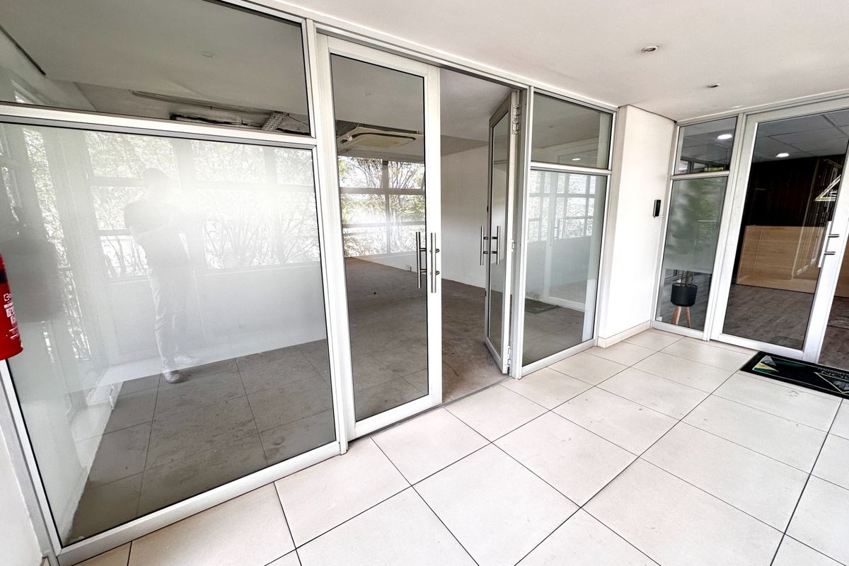 A bright, empty office space featuring modern glass partitions, aluminum framing, and clean tiled flooring, suitable for a professional workspace layout.