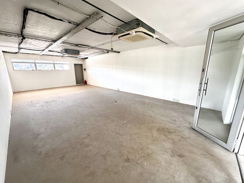 An empty, open-plan office space featuring an exposed ceiling with ducted air conditioning, concrete flooring, and a modern glass entrance door.