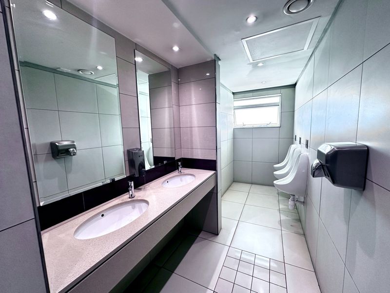 Modern office restroom featuring a dual vanity with stone countertop, tiled finishes, and multiple wall-mounted urinals.
