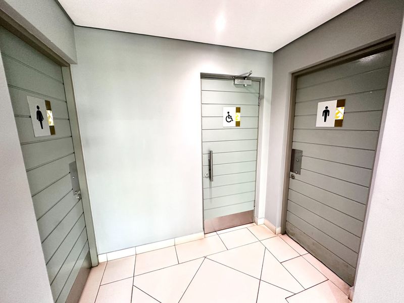 A clean, well-maintained office hallway featuring tiled flooring and clearly marked accessible and gender-specific restroom facilities.