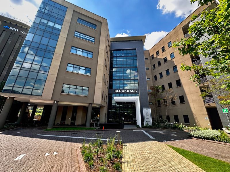 A modern multi-story office building facade featuring glass curtain walls, a paved driveway, and a professional entrance area.