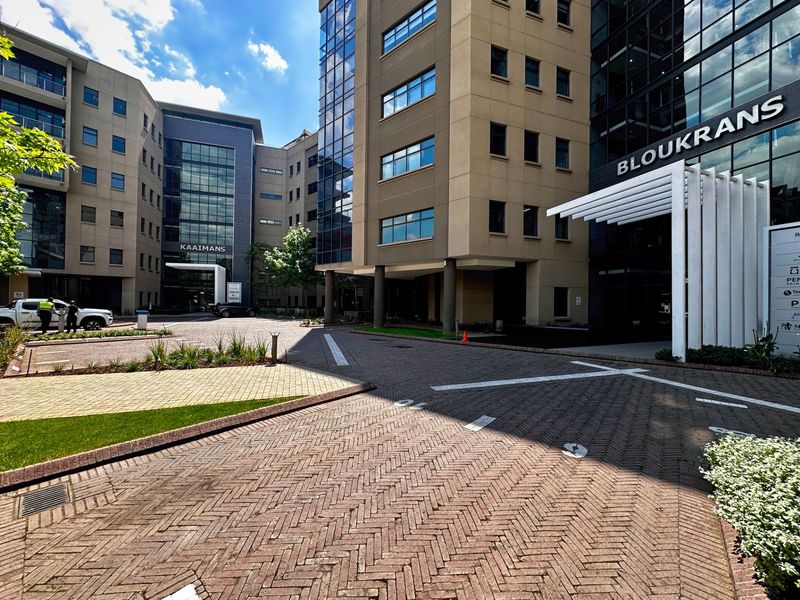 Modern commercial office complex exterior featuring paved driveway access, glass facade elements, and a prominent entrance canopy.