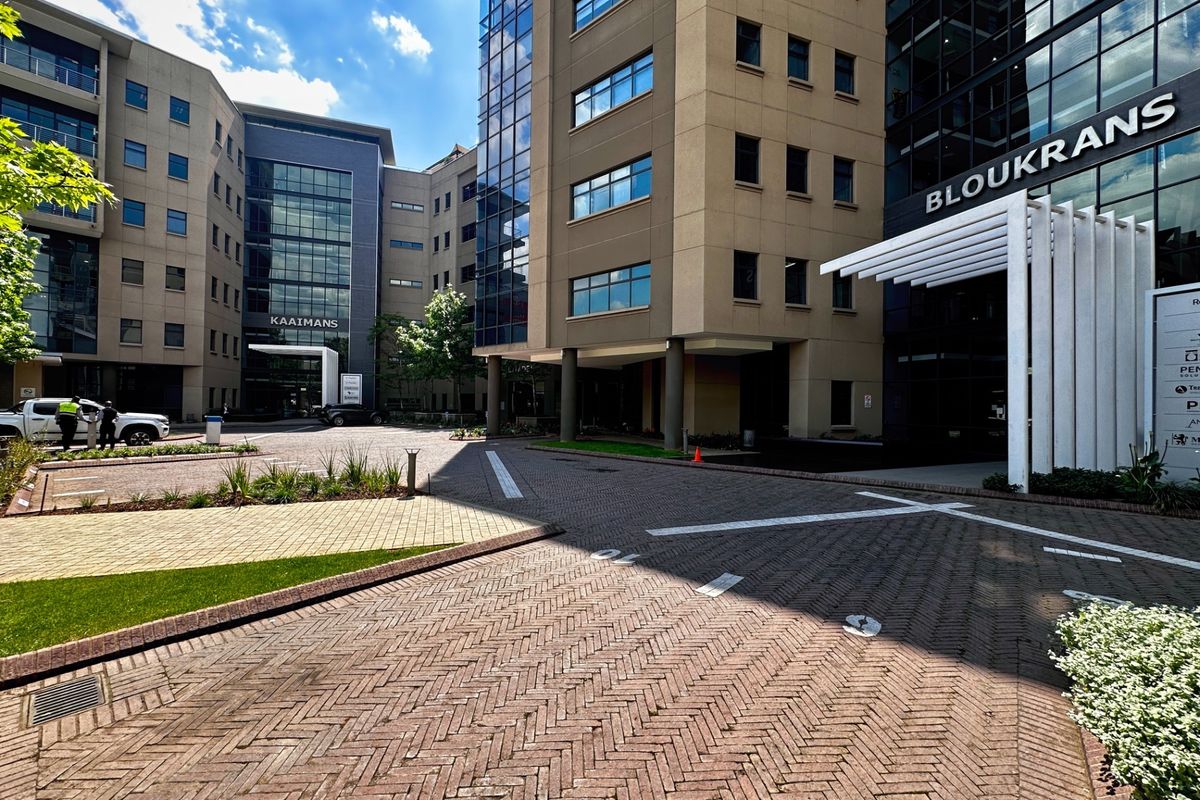 Modern commercial office complex exterior featuring paved driveway access, glass facade elements, and a prominent entrance canopy.