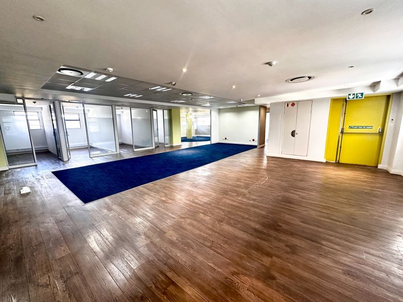Spacious open-plan office area featuring glass partitions, a mix of laminate and carpet flooring, and recessed ceiling lighting.