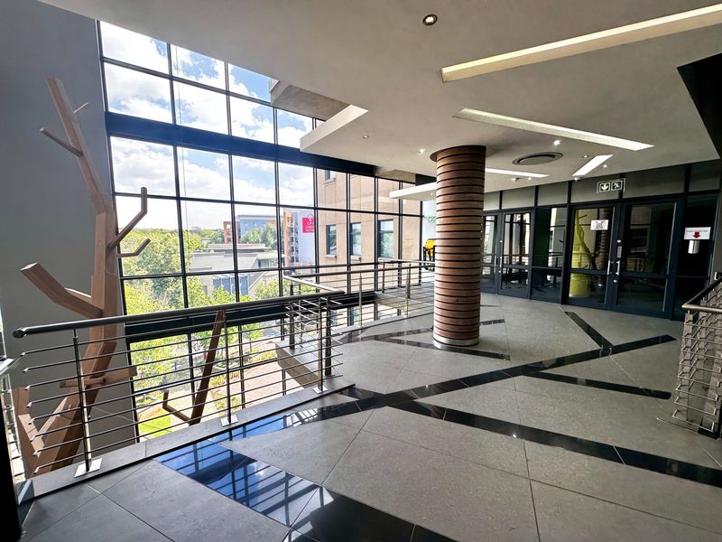 Modern office building hallway featuring expansive floor-to-ceiling windows, high-quality tiled flooring, and a contemporary structural column design.