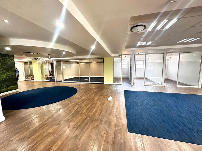 Spacious open-plan office area featuring modern glass partitions, recessed lighting, and a combination of wood-look flooring and carpeted zones.
