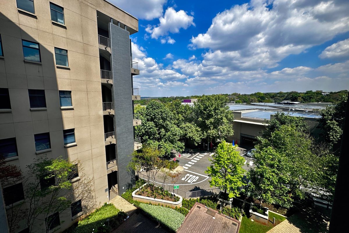 An elevated view of the office building exterior, featuring a multi-story facade, paved parking area, and landscaped grounds.