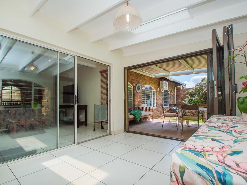 A bright, enclosed patio area featuring tiled flooring, exposed beam ceilings with skylights, and seamless indoor-outdoor flow through large sliding and folding glass doors.
