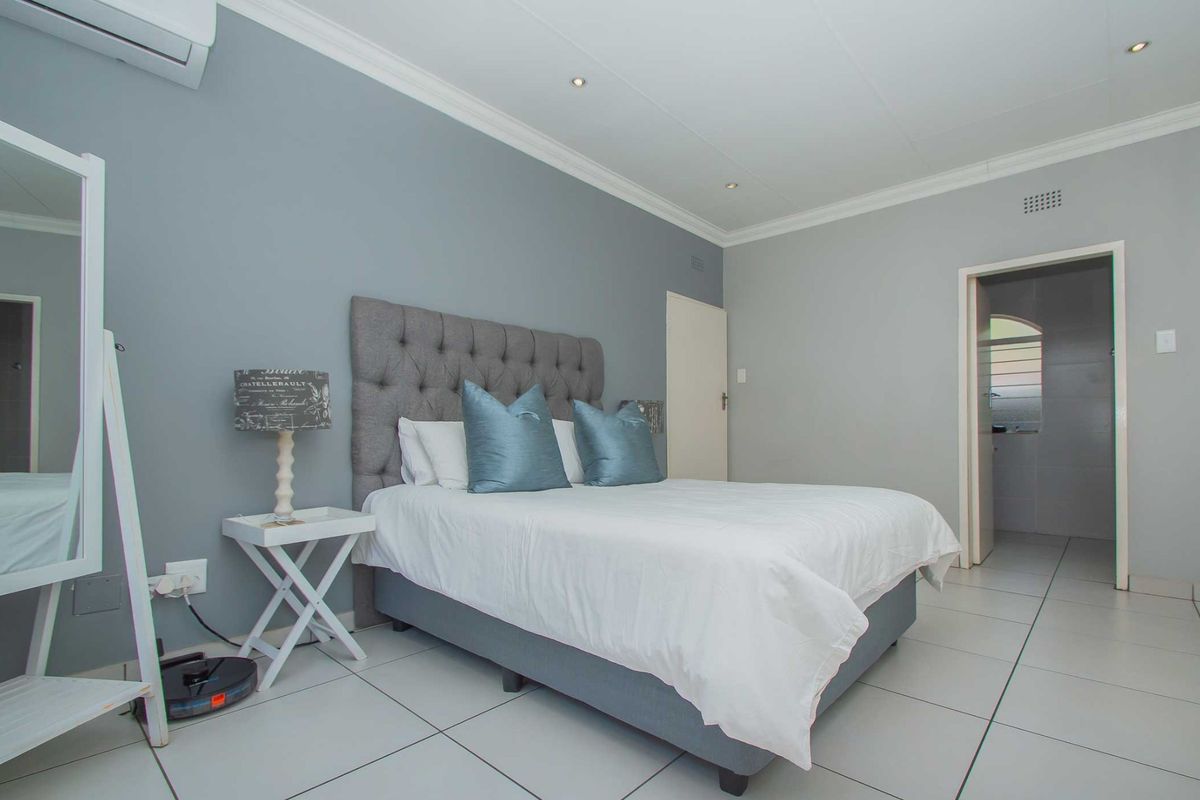 A well-maintained bedroom featuring neutral grey walls, tiled flooring, recessed downlighting, and an integrated air conditioning unit.