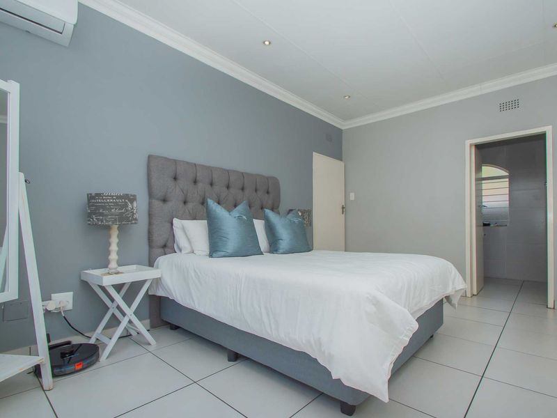 A well-maintained bedroom featuring neutral grey walls, tiled flooring, recessed downlighting, and an integrated air conditioning unit.