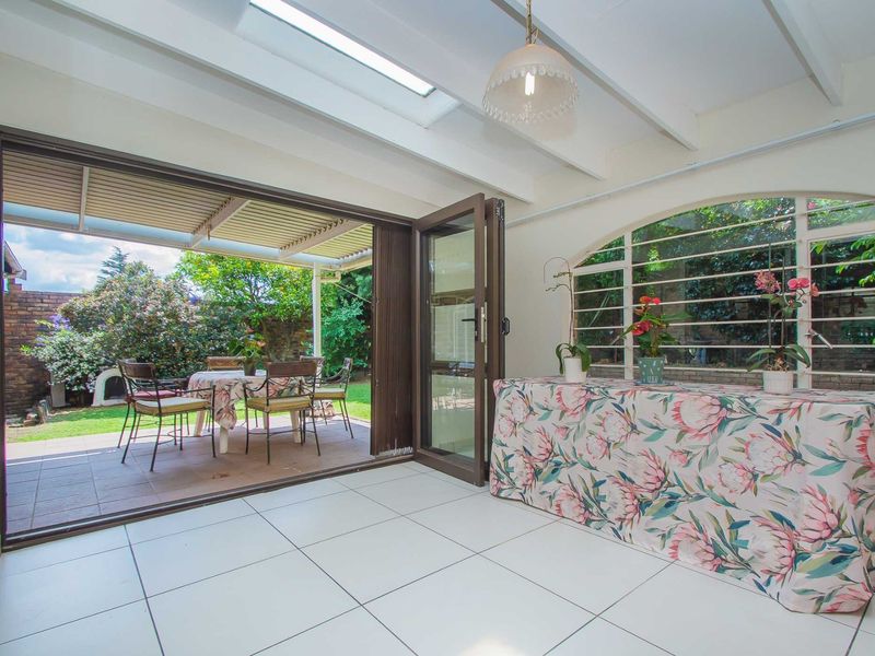 A bright sunroom featuring tiled floors, skylights, and exposed beams, with folding doors opening onto a covered patio and garden area.