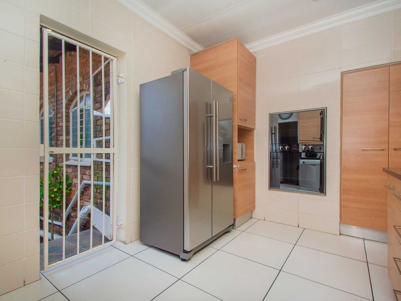 A functional kitchen featuring light wood cabinetry, tiled surfaces, and a built-in oven, with direct access to an exterior area via a security gate.