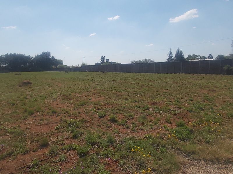 A vacant residential plot featuring a perimeter wall and access to an unpaved road, offering a clear space for future development.