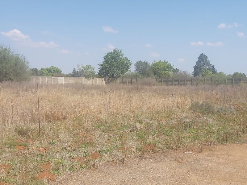 A vacant residential plot featuring natural grass cover, an unpaved access track, and a precast concrete boundary wall along the rear perimeter.