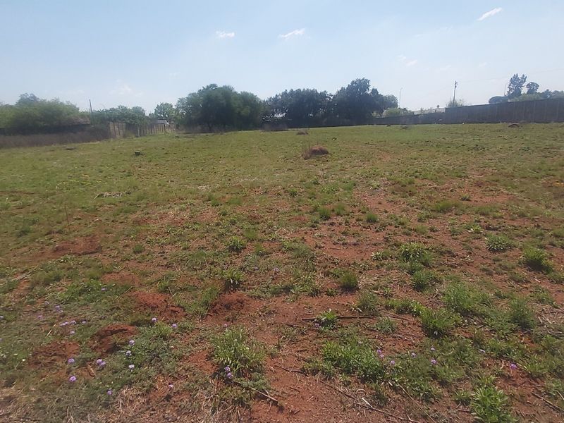 A wide-angle view of a vacant residential plot featuring natural grass cover and a perimeter boundary wall.