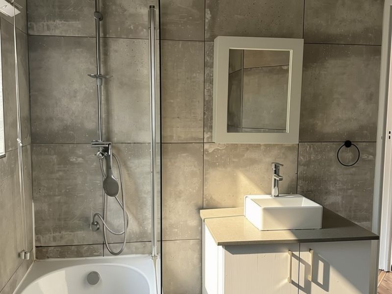 Modern bathroom featuring a bathtub with a glass screen, a vessel sink vanity, and contemporary concrete-look wall tiling.
