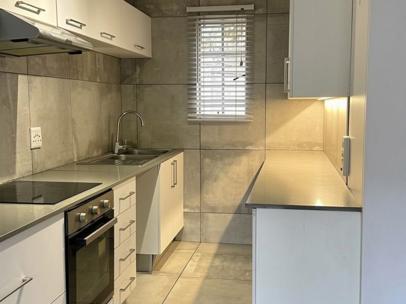 A modern, clean kitchen featuring white cabinetry, stainless steel appliances, tiled walls, and ample counter space, illuminated by under-cabinet lighting.