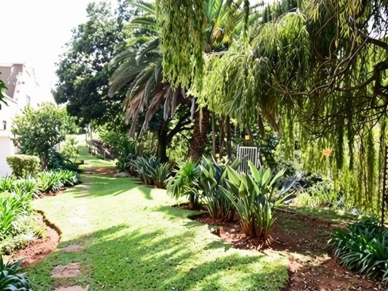 A lush, well-maintained garden featuring mature trees, established tropical plants, and a stone pathway leading through the landscaped grounds.