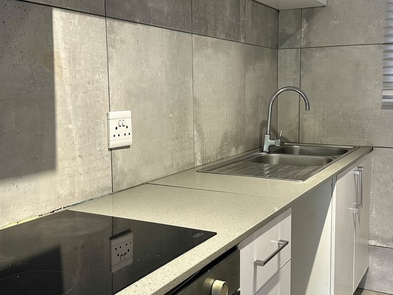A modern kitchen featuring a sleek stone countertop, built-in electric hob and oven, stainless steel sink, and contemporary tiled backsplash.