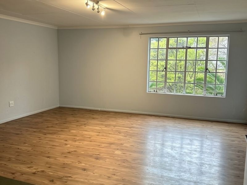 A spacious, empty living room featuring laminate wood flooring, a large multi-pane window, and modern ceiling-mounted spotlighting.