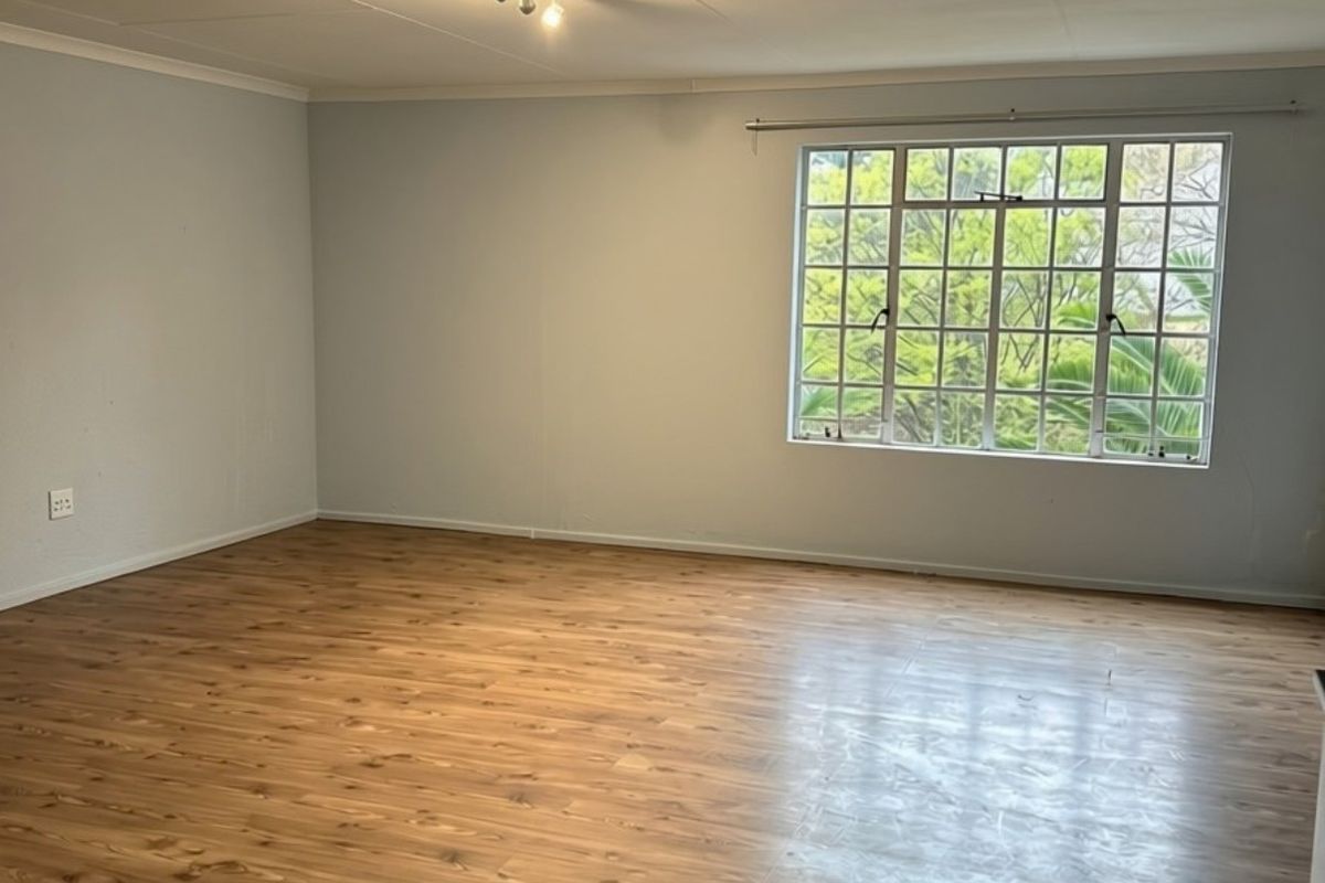 A spacious, empty living room featuring laminate wood flooring, a large multi-pane window, and modern ceiling-mounted spotlighting.