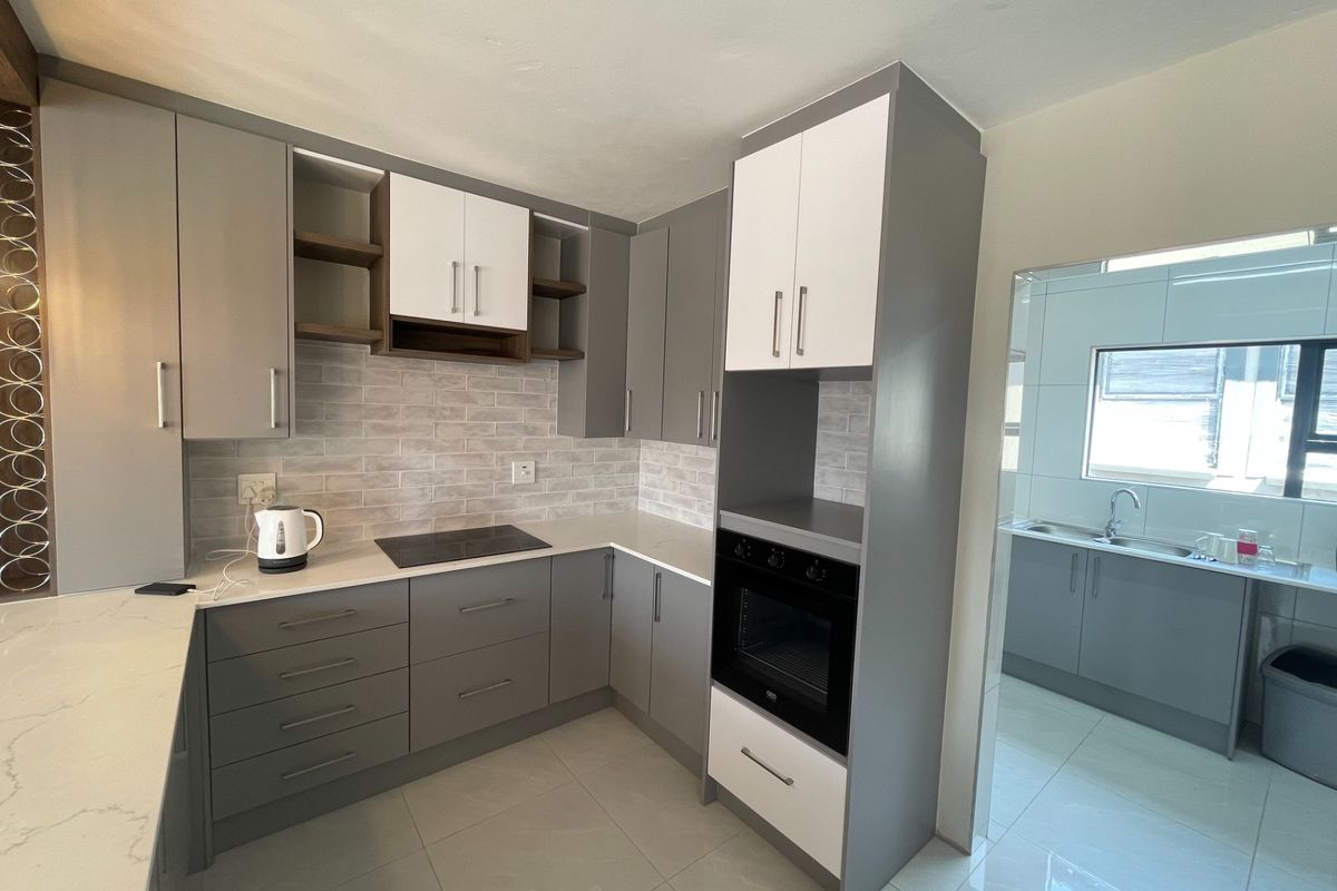 Modern kitchen featuring grey and white cabinetry, stone countertops, built-in oven, electric hob, and a subway tile backsplash, with an adjacent scullery area.