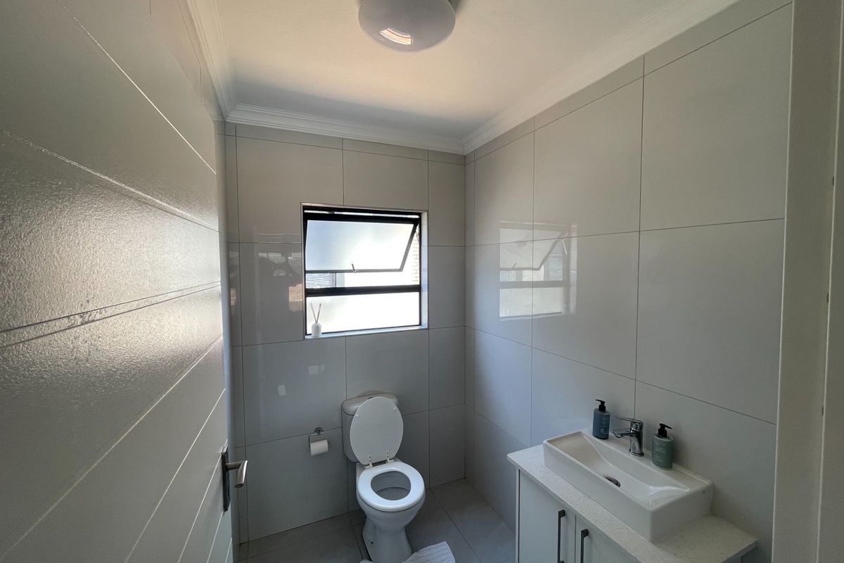 A modern, well-maintained bathroom featuring floor-to-ceiling wall tiles, a sleek vanity with basin, and a functional top-hung window for ventilation.