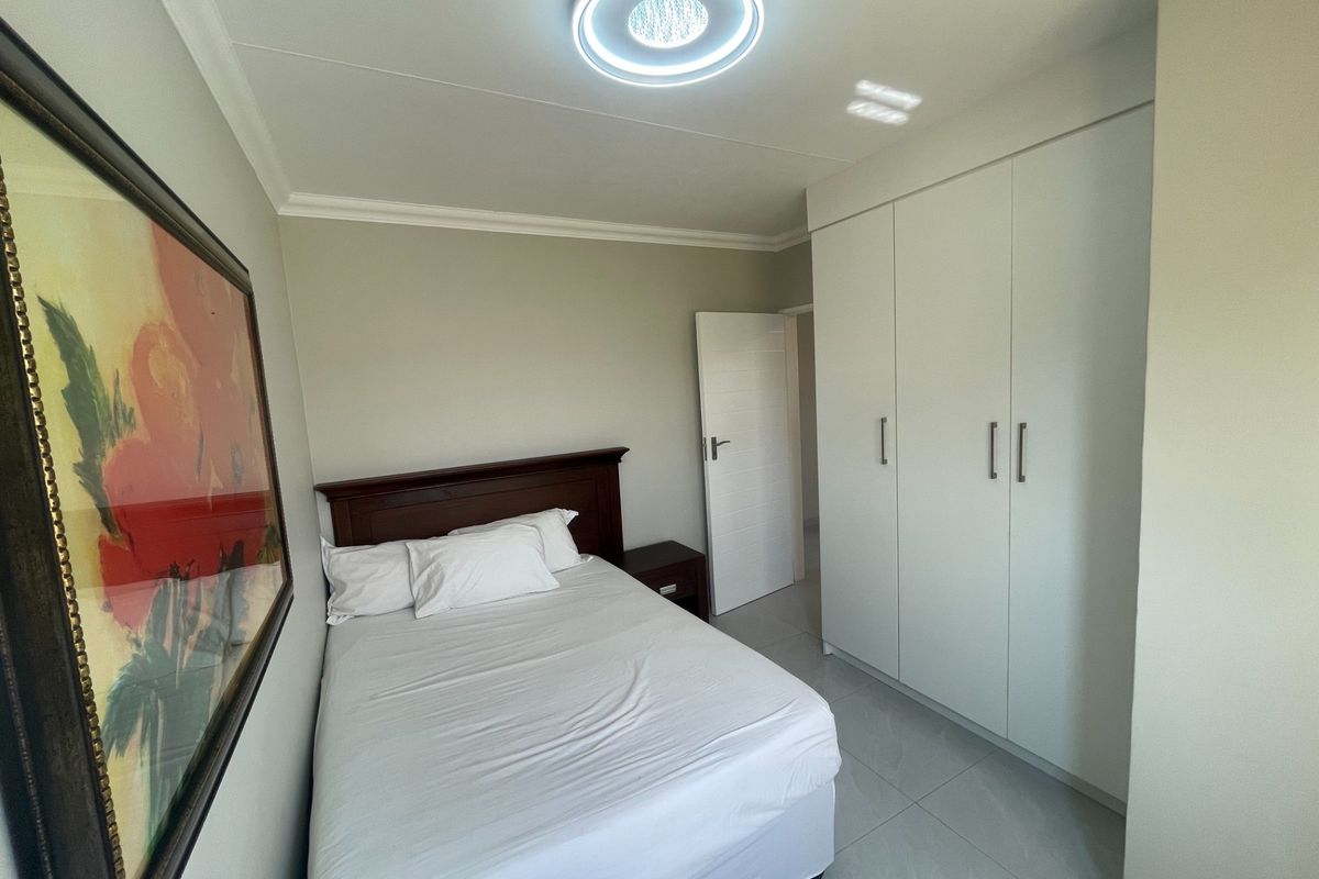 A well-maintained bedroom featuring neutral tiled flooring, built-in white cupboards, and a modern ceiling light fixture.