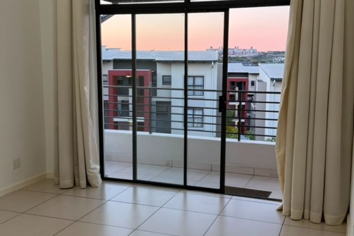 Bright and spacious living area featuring neutral tiled flooring and large sliding glass doors that open onto a private balcony with sunset views.