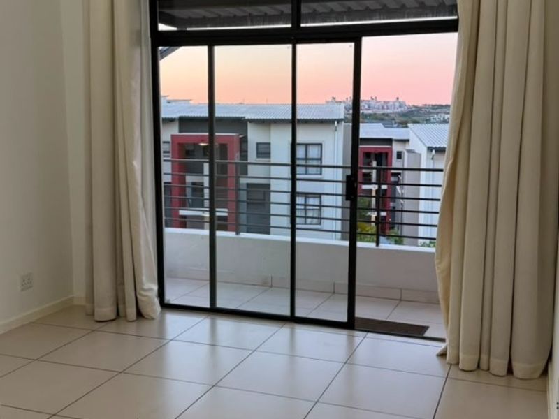 Bright and spacious living area featuring neutral tiled flooring and large sliding glass doors that open onto a private balcony with sunset views.