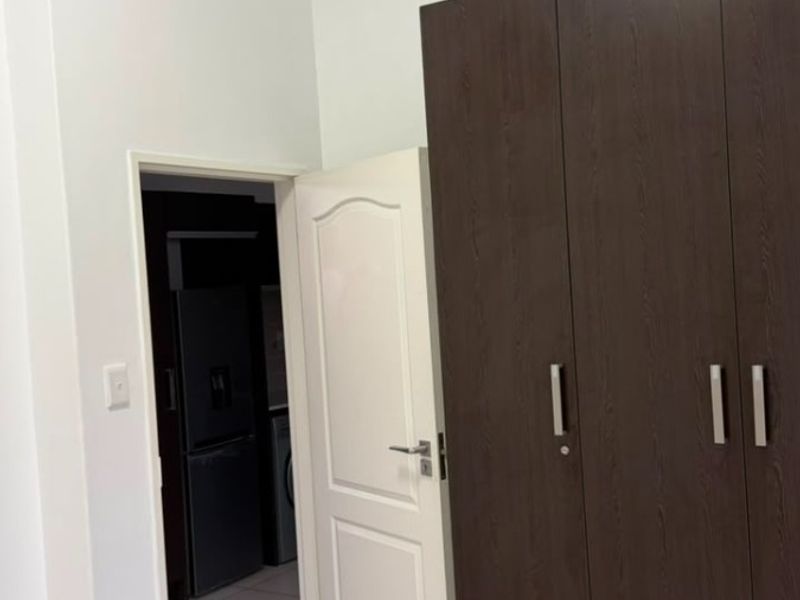 A clean bedroom featuring neutral tiled flooring and a large, dark wood-finish built-in wardrobe, with an adjacent doorway leading to another room.