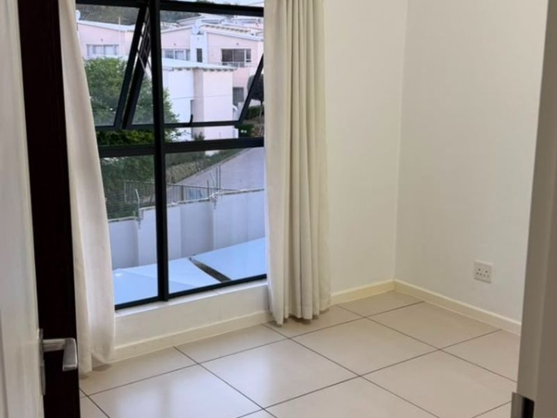 A bright, empty bedroom featuring neutral tiled flooring, clean white walls, and a large aluminium-framed window with natural light.