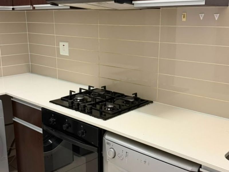 A functional kitchen featuring dark wood cabinetry, stone countertops, a gas hob, built-in oven, and a tiled backsplash.