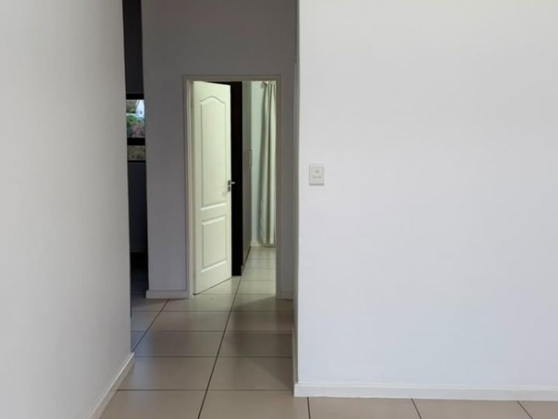 A clean, neutral hallway featuring light-colored floor tiles and white walls, providing a bright and open transition between rooms.