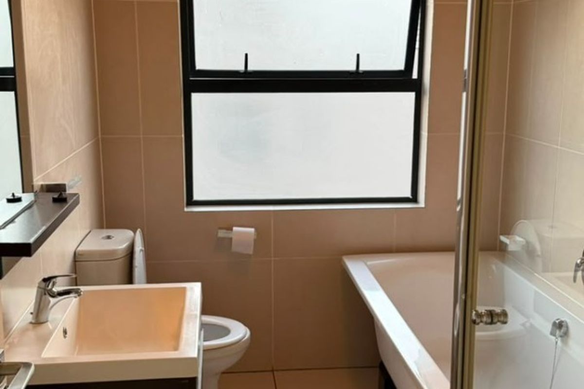 A clean, modern bathroom featuring a vanity basin, toilet, bathtub, and a separate shower enclosure with neutral wall and floor tiling.