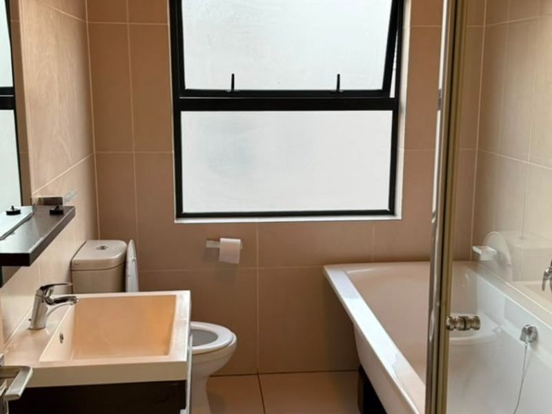 A clean, modern bathroom featuring a vanity basin, toilet, bathtub, and a separate shower enclosure with neutral wall and floor tiling.