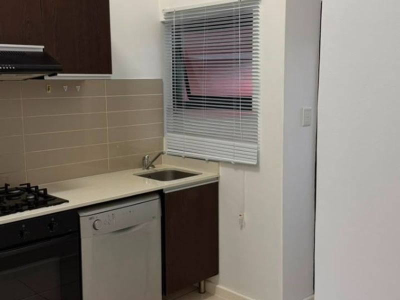 Compact kitchen featuring dark wood cabinetry, gas hob, oven, extractor fan, and tiled splashback with neutral floor tiles.