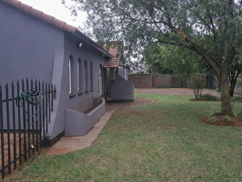 Rear exterior view of the property featuring a grey rendered facade, arched windows, terracotta roof tiles, and a landscaped garden with wrought iron fencing.