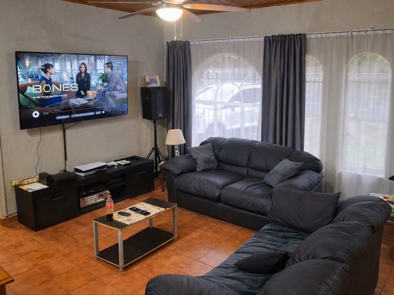A comfortable living room featuring tiled flooring, a timber ceiling, a ceiling fan, and large arched windows that allow natural light into the space.