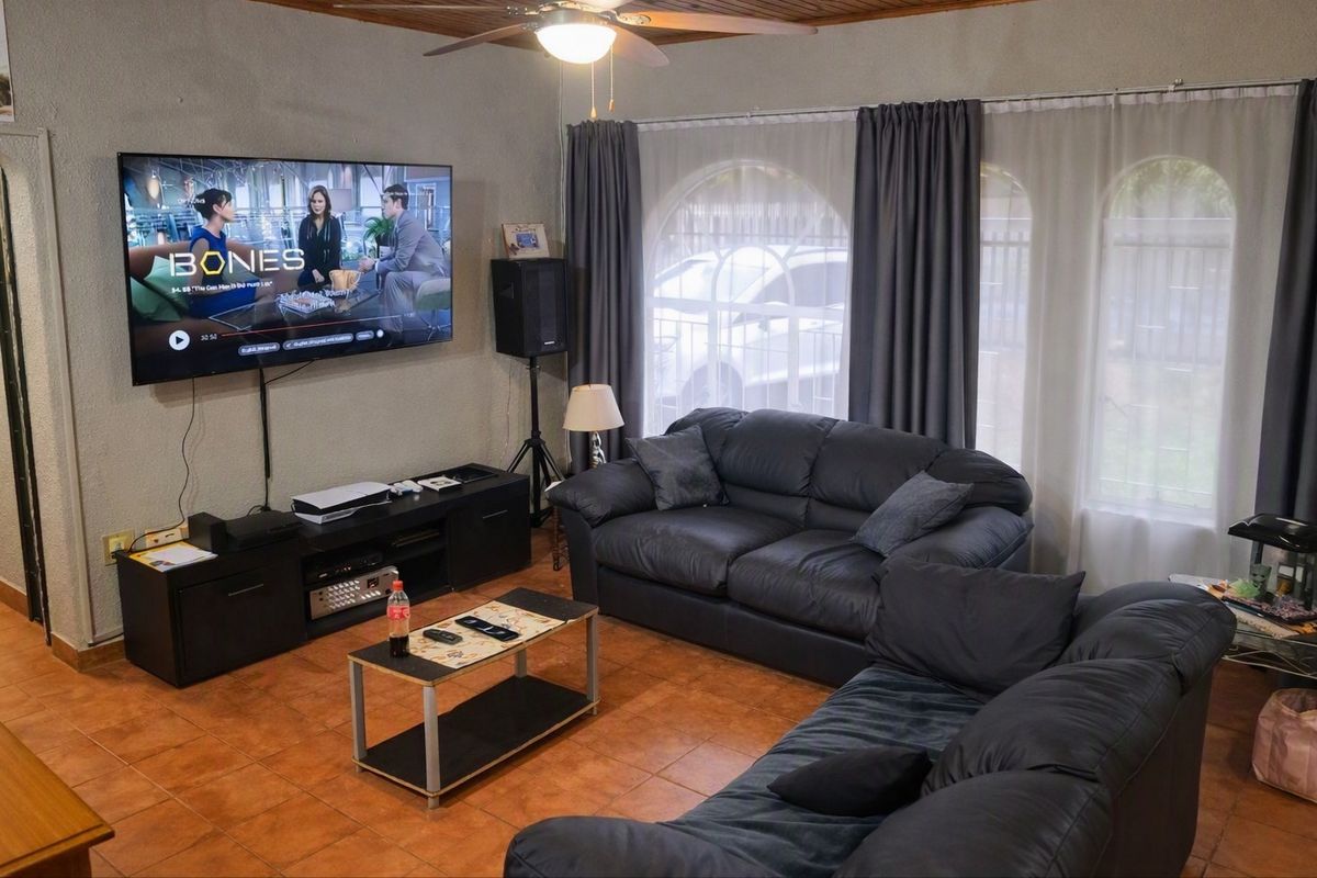 A comfortable living room featuring tiled flooring, a timber ceiling, a ceiling fan, and large arched windows that allow natural light into the space.