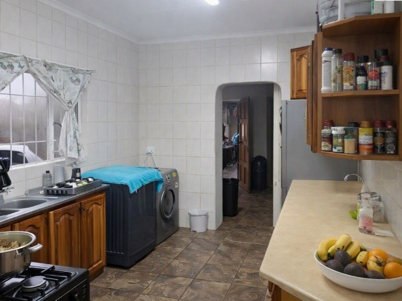 A functional scullery area featuring tiled walls, laminate countertops, built-in wooden cabinetry, and a stainless steel sink with dedicated laundry appliance space.