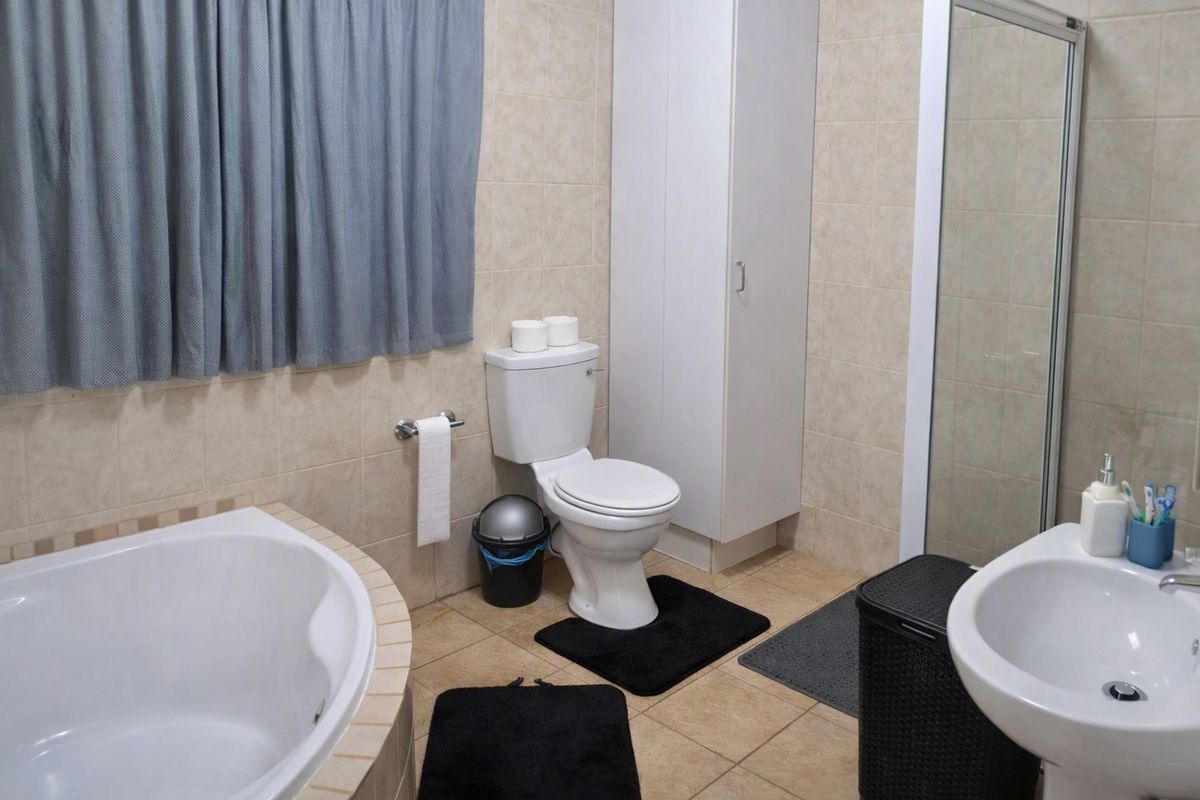 A functional bathroom featuring a built-in bathtub, separate shower enclosure, pedestal washbasin, toilet, and a tall built-in storage cabinet with tiled finishes.