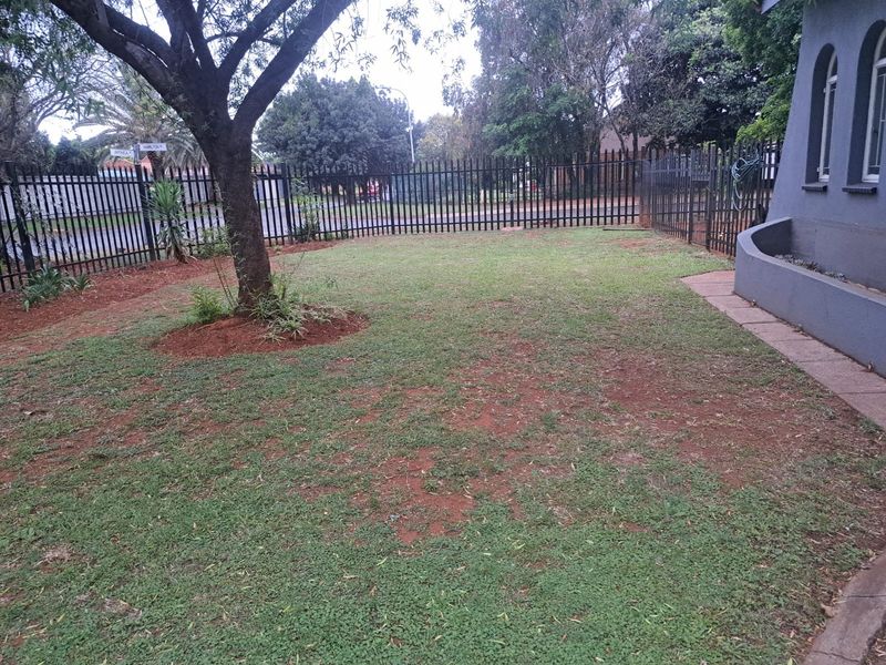 A private garden area featuring a mature tree, paved walkway, and metal perimeter fencing, offering potential for landscaping improvements.