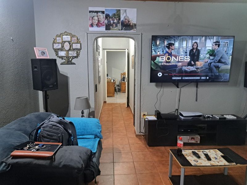 A living room featuring tiled flooring and an arched doorway leading to an adjacent room, with a wall-mounted television and textured wall finishes.